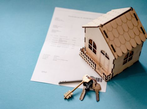 Ein Modellhaus steht auf einem Kaufvertrag. Daneben liegt ein Schlüssebund mit einem Hausschlüssel.